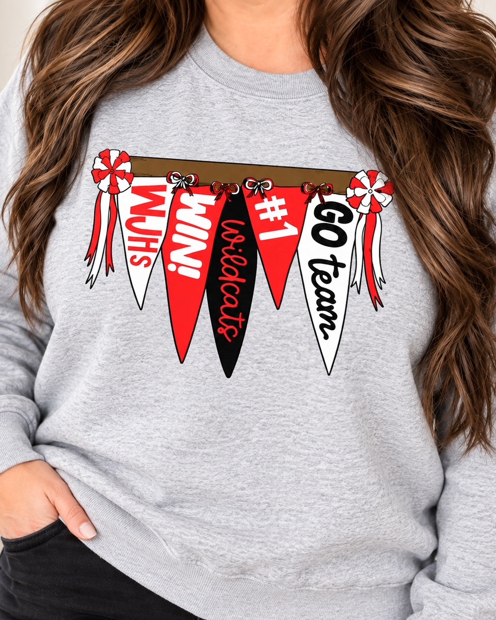 Brunette woman wearing the sport gray Wildcat Rally Girl sweatshirt with red, black, and white pennant artwork.
