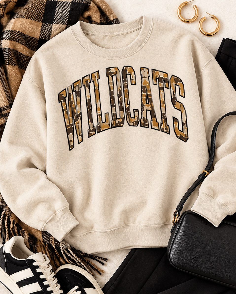 Sand Wildcat Territory sweatshirt styled with black pants, a camel plaid scarf, black sneakers, and a black crossbody bag.