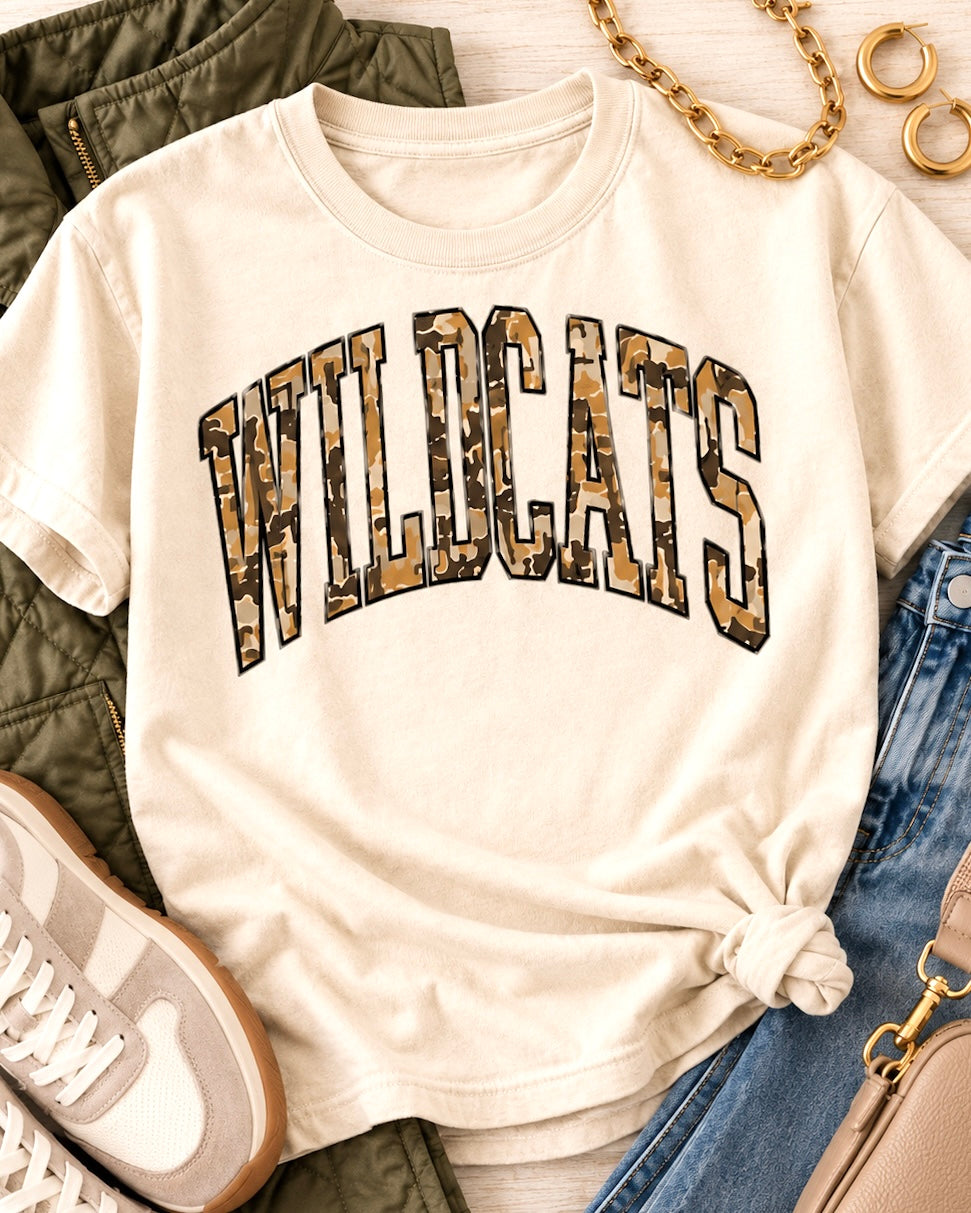 Wildcat Territory tee styled with an olive quilted vest, distressed jeans, neutral sneakers, gold jewelry, and a taupe bag.