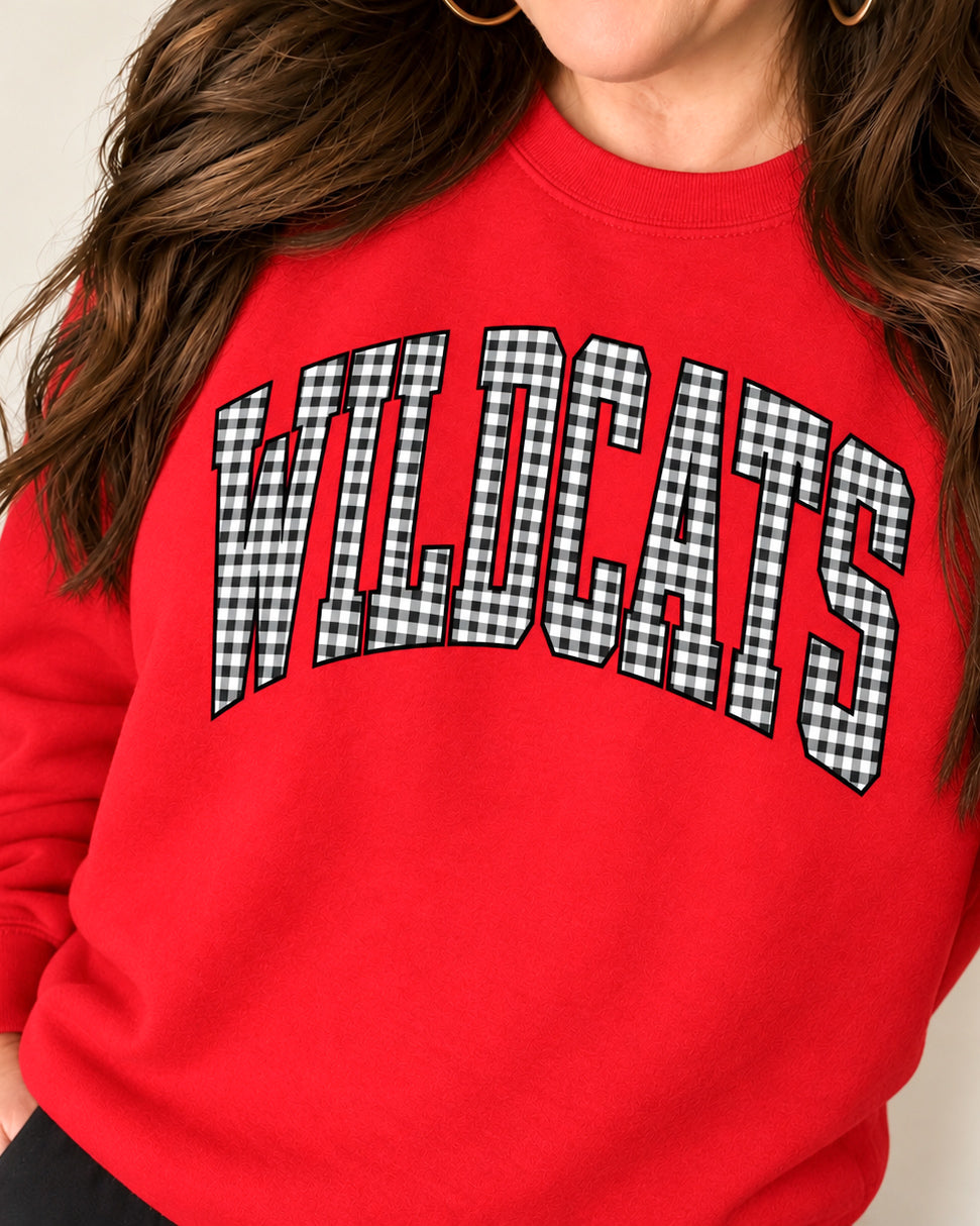 Woman modeling the red Wildcats crewneck sweatshirt with black-and-white gingham lettering and gold hoop earrings.