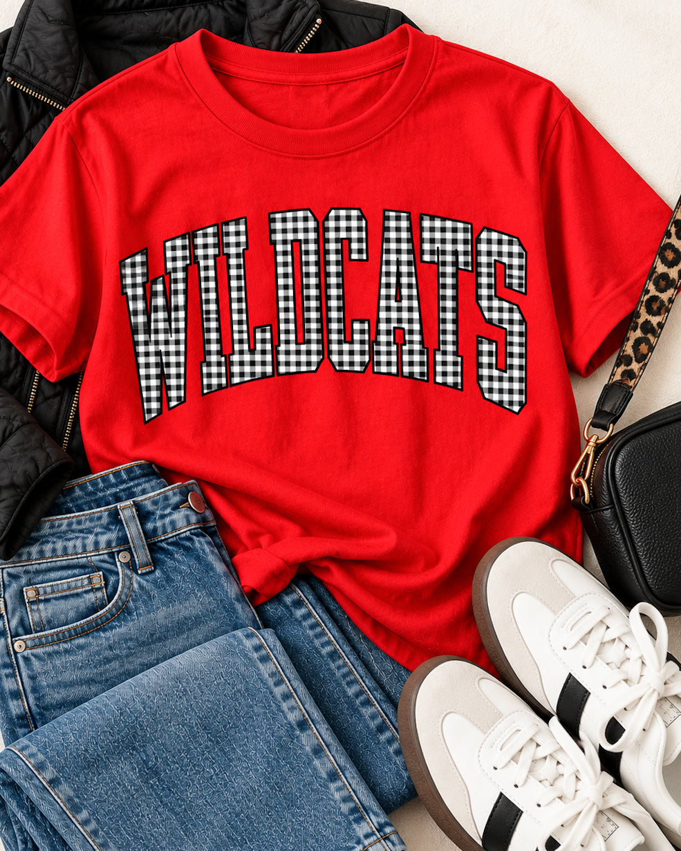 Red Wildcats gingham tee styled with jeans, a black quilted jacket, retro sneakers, and a black crossbody bag.