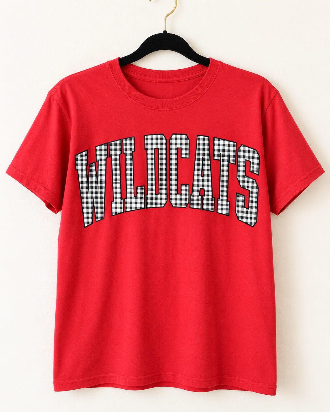 Red Wildcats short-sleeve tee with black-and-white gingham lettering on a black velvet hanger.