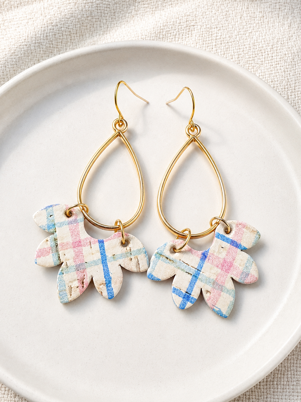 Wildflower Patch handmade cork earrings with pastel plaid cork, genuine leather backing, and gold-tone teardrop accents displayed on a white ceramic dish.