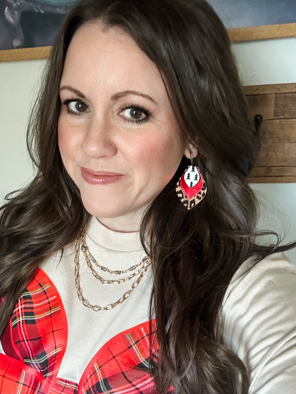 Model wearing the small Wildwood Noel Earrings featuring layered leopard print, red shimmer, and pine tree cork on hoops, paired with the Christmas Morning Long-Sleeve Tee.
