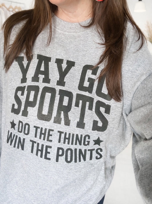 Woman wearing heather gray graphic sweatshirt with black lettering that reads Yay Go Sports Do the Thing Win the Points.