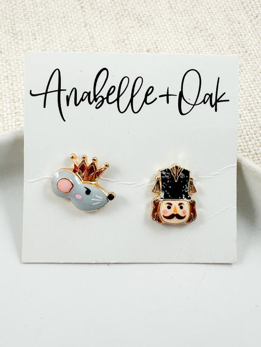Small stud earrings on a display card showing a crowned mouse head and a Nutcracker head in soft winter colors.